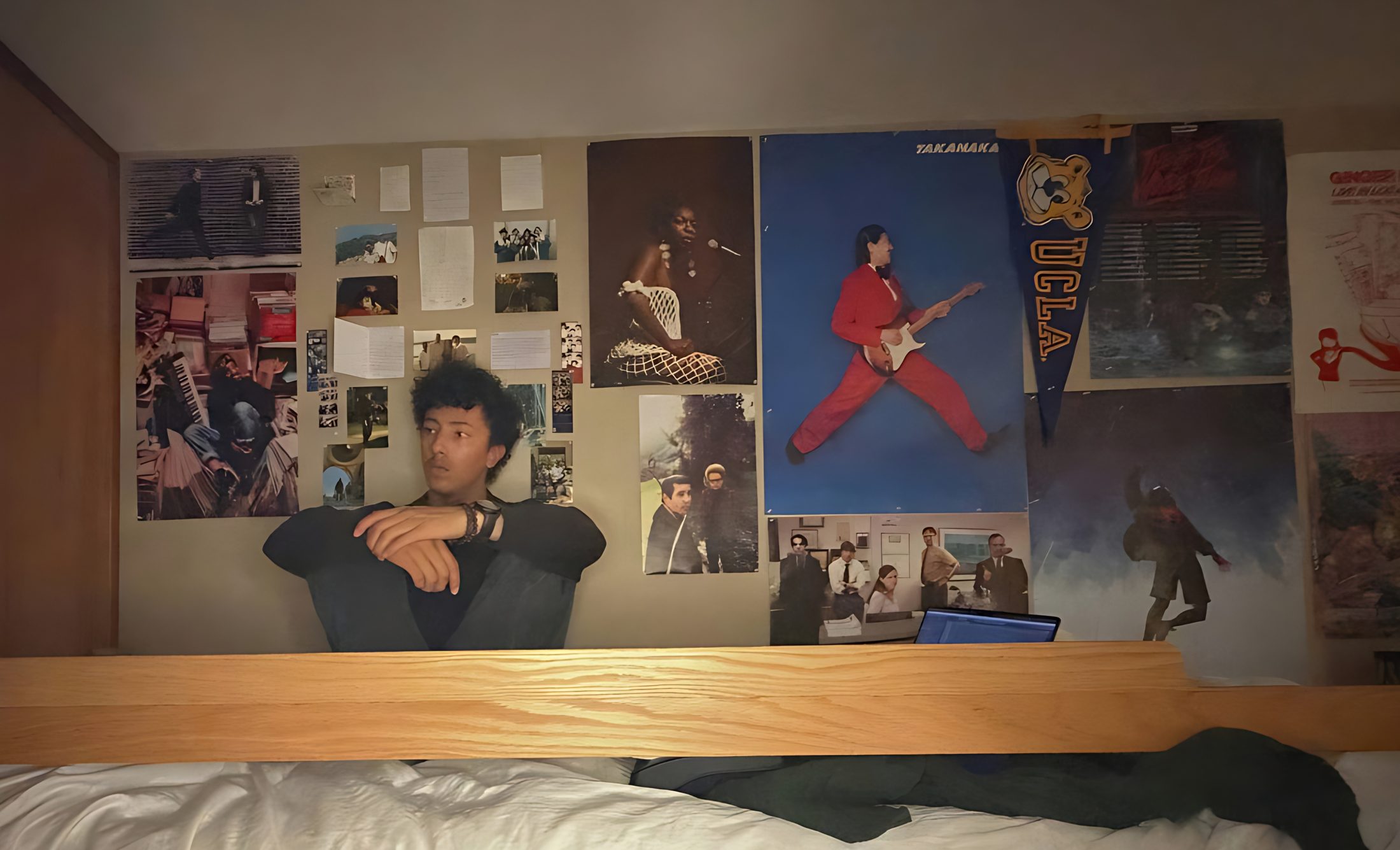 Nahoa Life sitting on his bed against a wall of posters